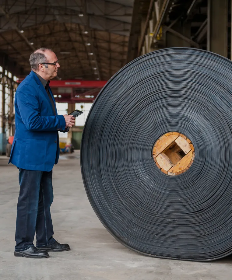 Man in a suit beside a large industrial roll of rubber material