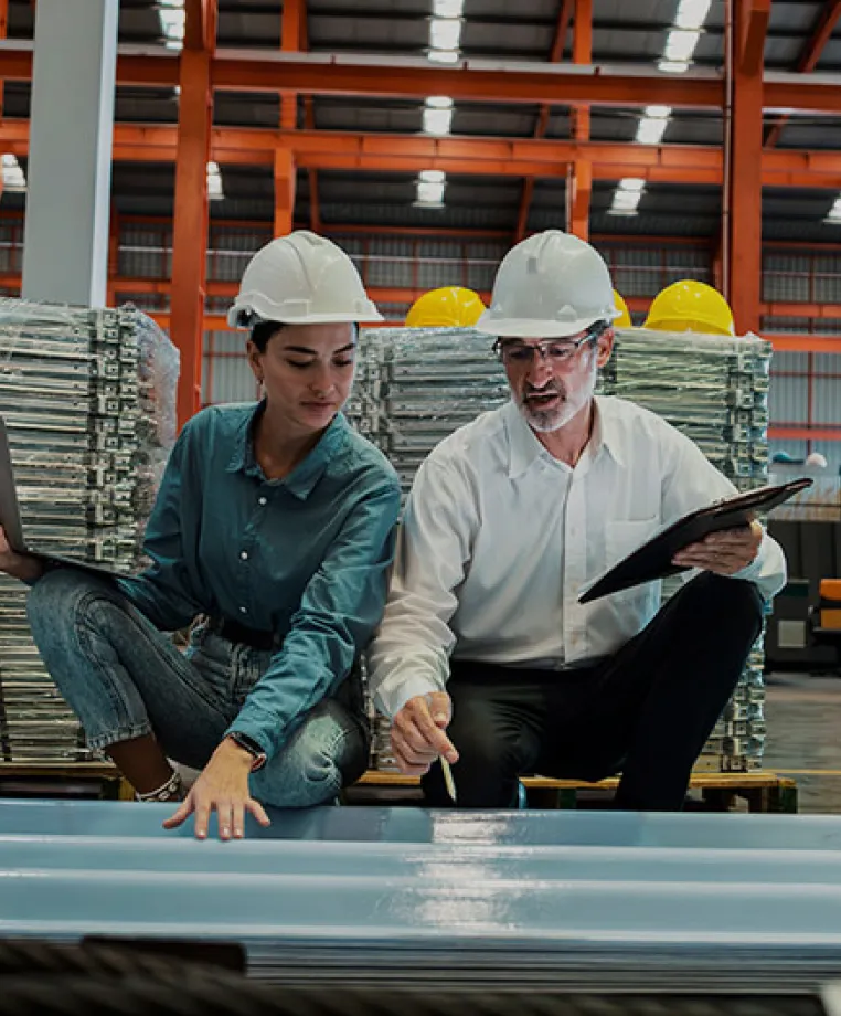 Two workers in hard hats inspecting metal stock in a warehouse