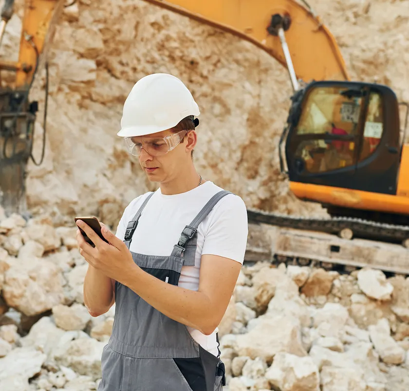 Construction worker using a phone in front of an excavator on a demolition site