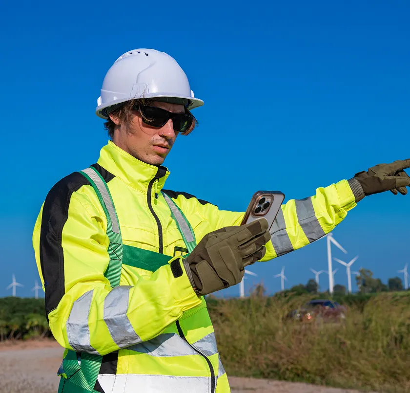 Worker in a hi-vis jacket using a phone at a wind farm