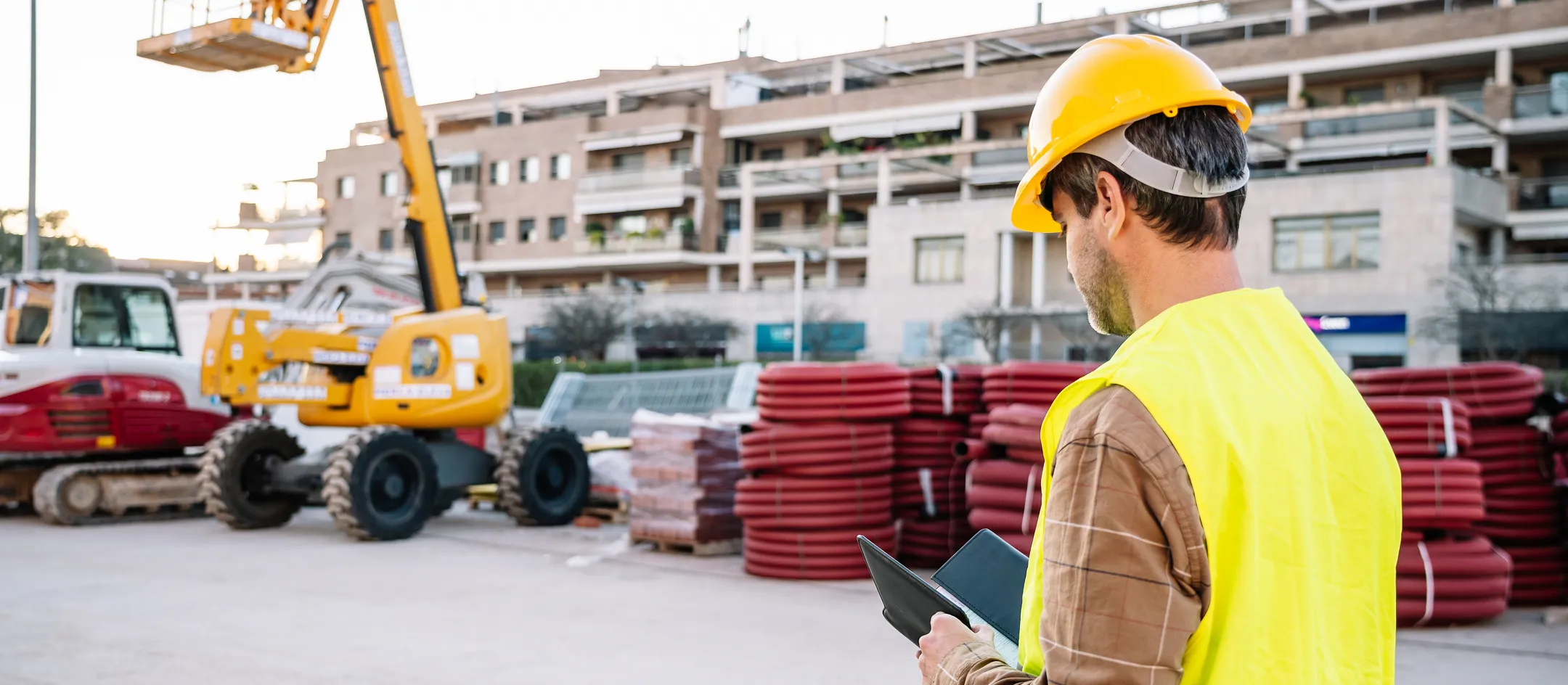 Worker in hi-vis using a tablet at a plant hire yard