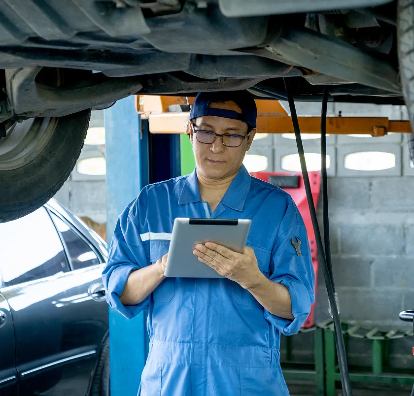 Mechanic in overalls using a tablet beneath a car on a ramp