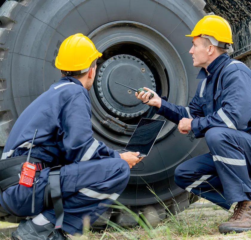 Two workers in hard hats inspecting a large truck wheel