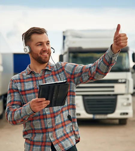 Smiling driver giving a thumbs up beside trucks