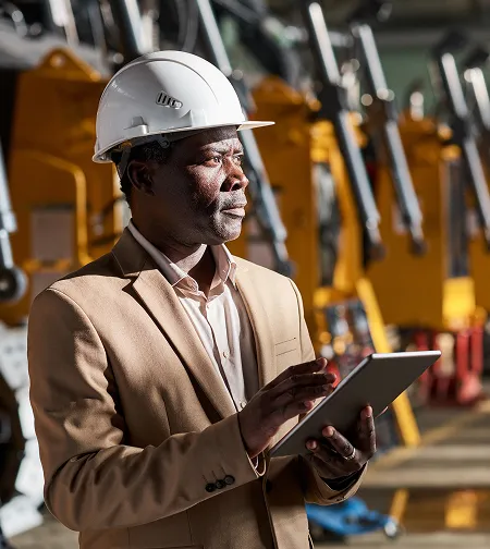 Businessman holding a tablet beside yellow machinery