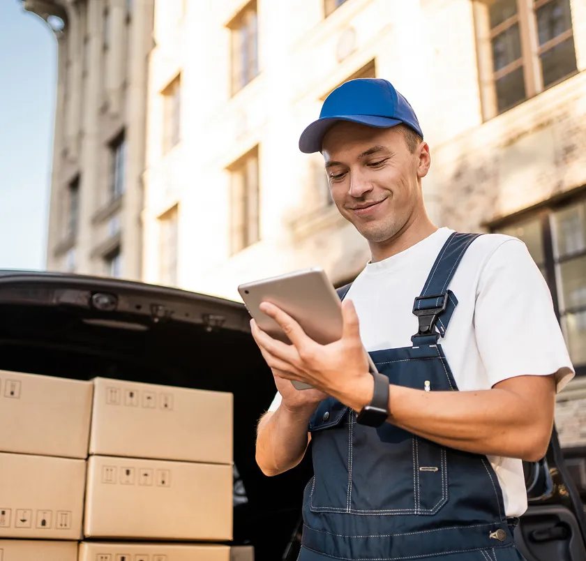 Worker in dungarees using a tablet beside stacked delivery boxes