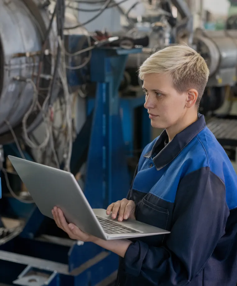 Worker using a laptop beside machinery