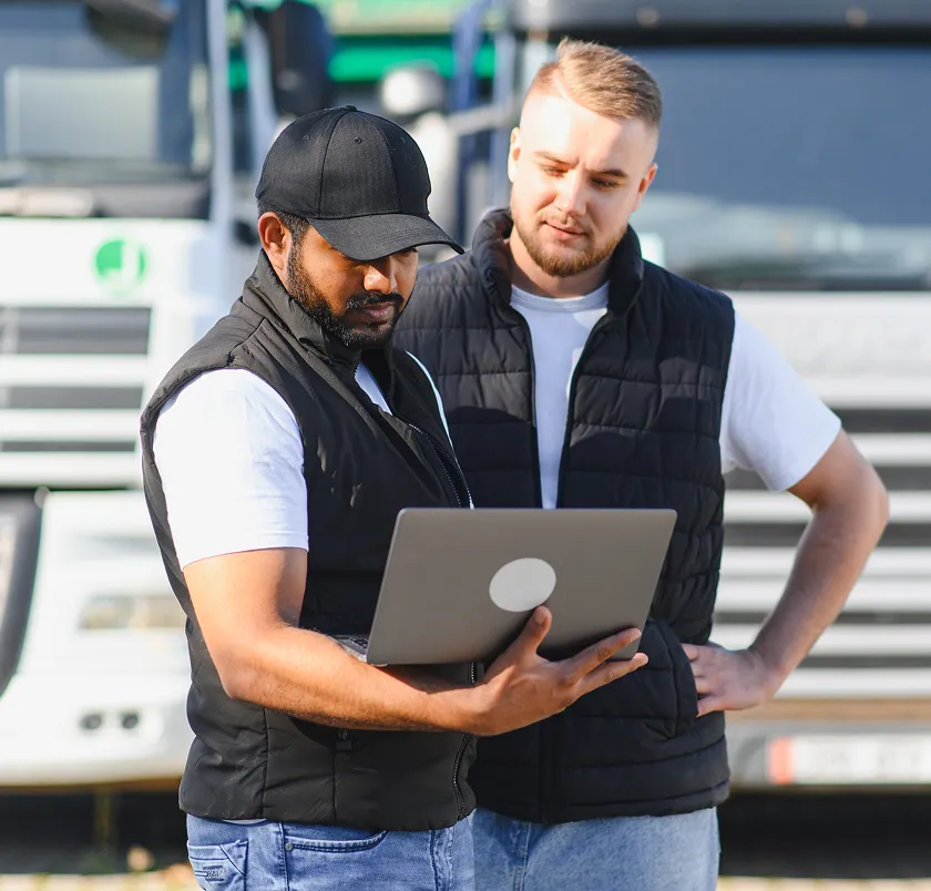 Two mechanics reviewing information on a laptop beside a truck
