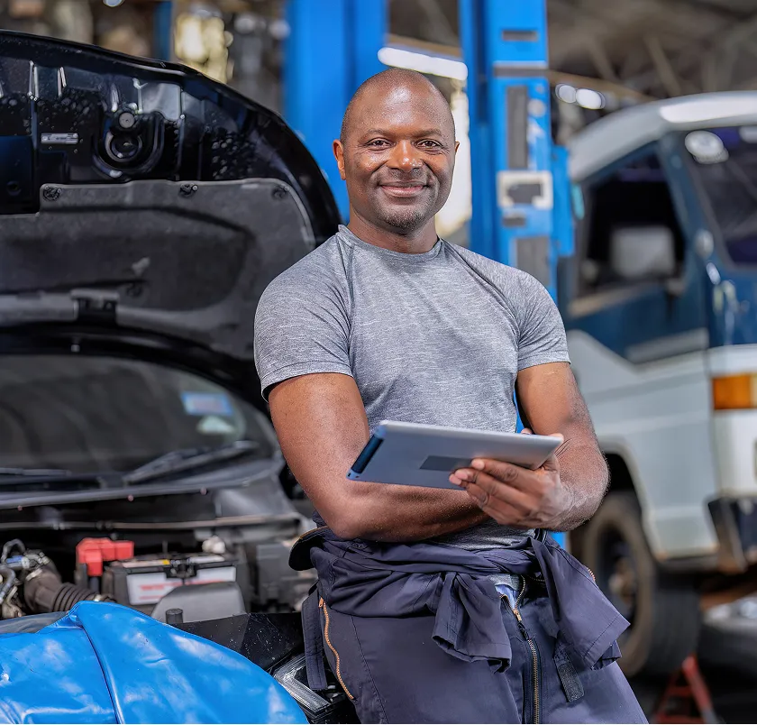 Smiling mechanic holding a tablet in front of a van with its bonnet open
