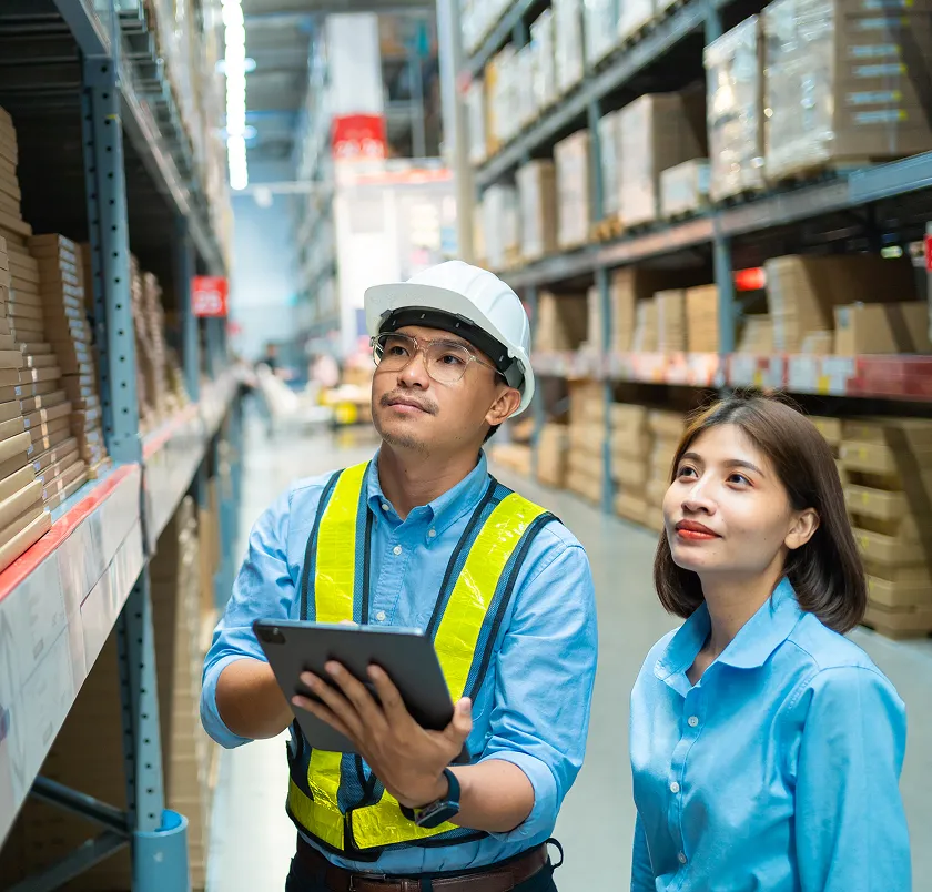 Warehouse workers in hard hats and hi-vis vests using a tablet to check stock