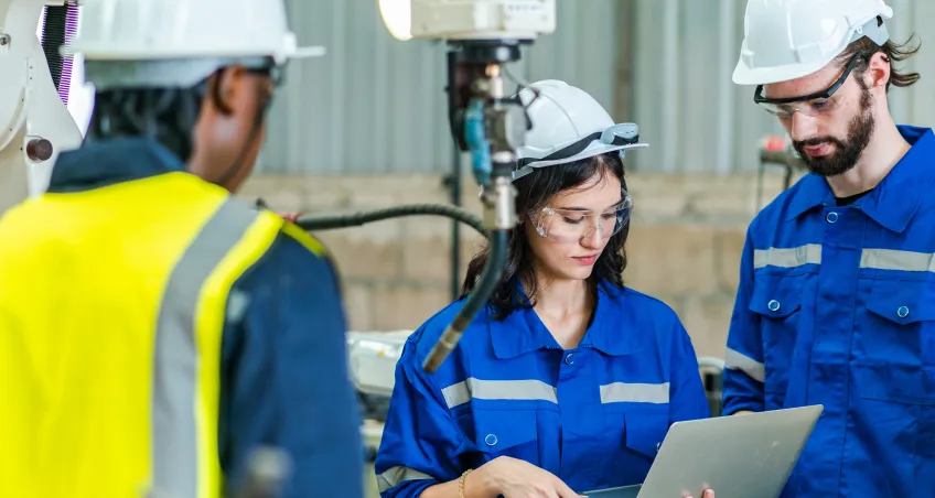 Engineers in hard hats inspecting equipment with a laptop