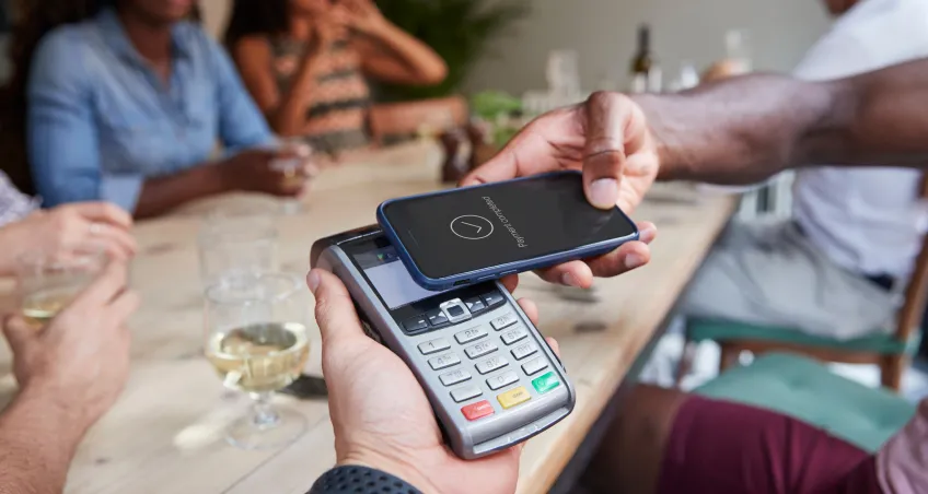 Diner making a contactless payment with a phone on a card terminal at a restaurant table