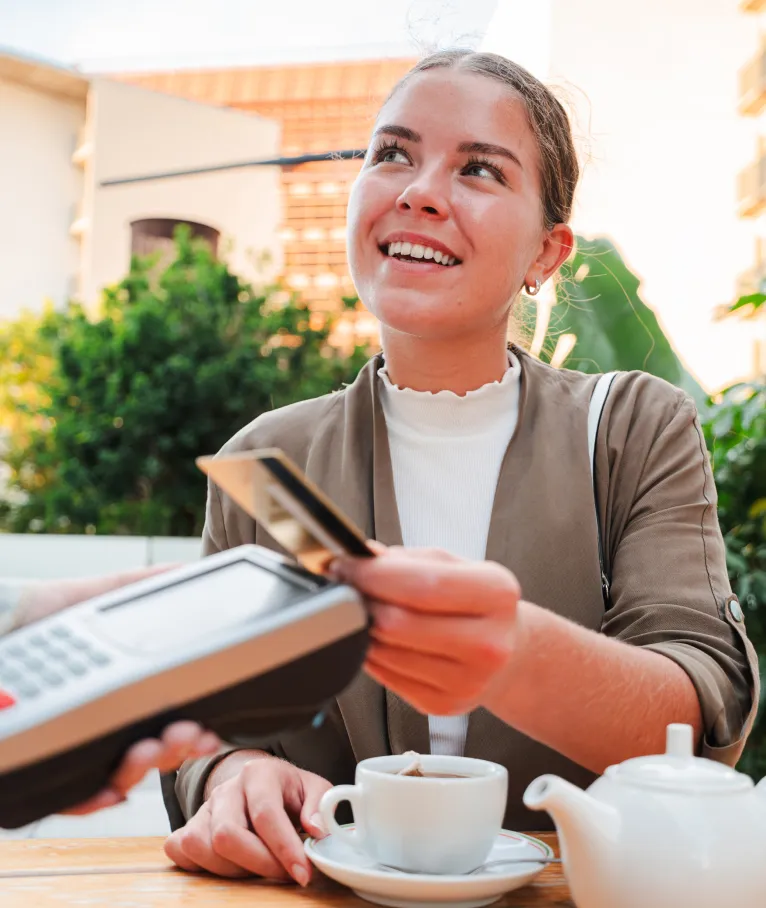 Smiling young woman paying by card on a payment terminal at an outdoor cafe