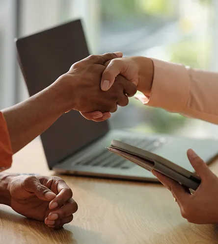 Close-up of two people shaking hands over a desk with a laptop