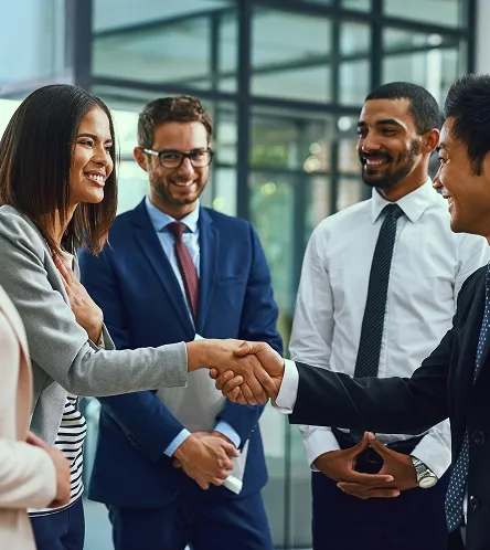Two business professionals shaking hands after a meeting as colleagues look on
