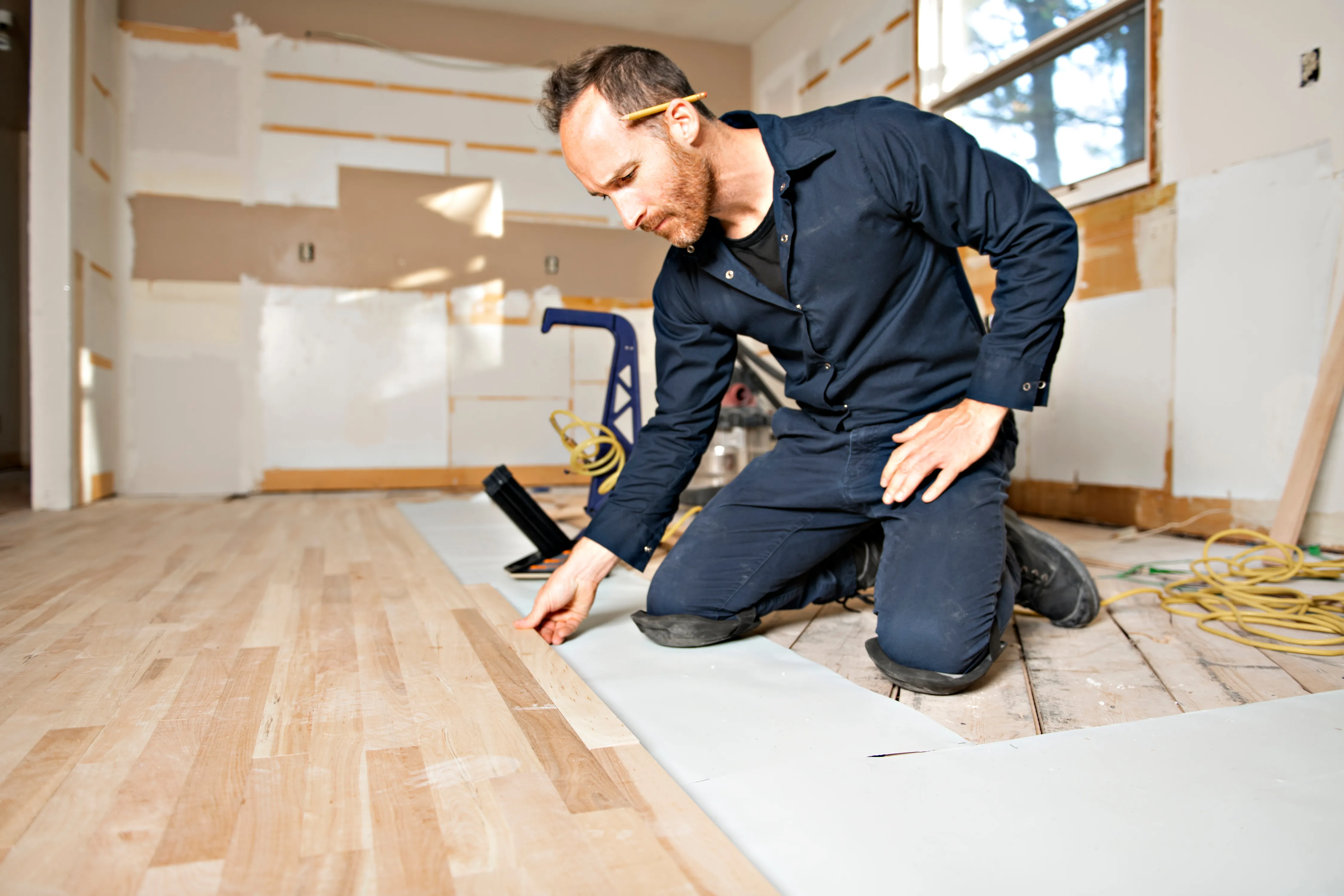 Tradesperson kneeling to lay hardwood flooring during a home renovation