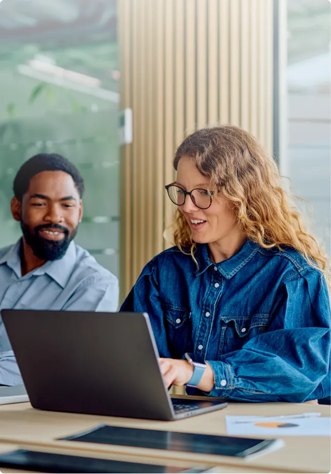 Two colleagues smiling at a laptop in an office