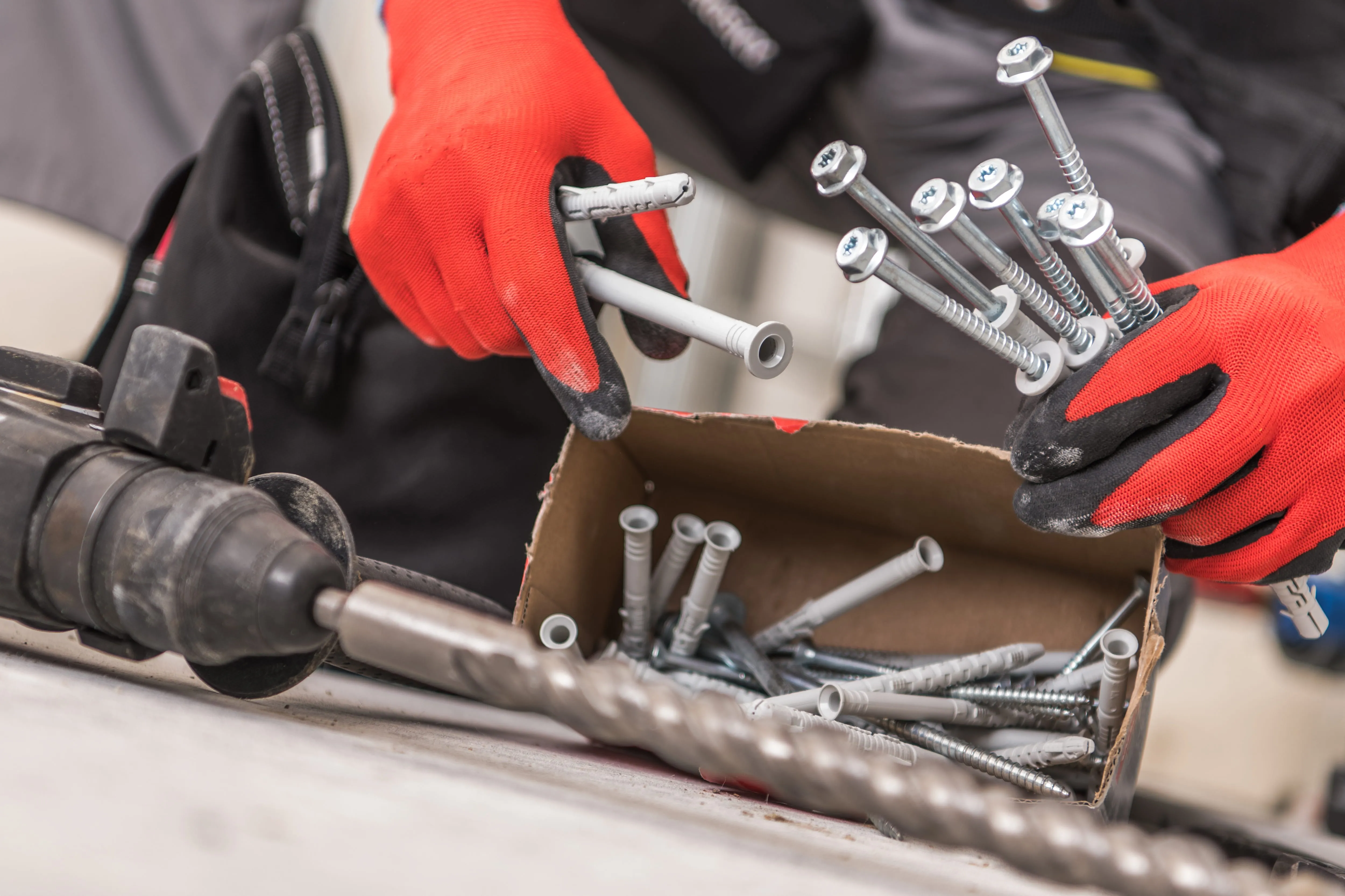 Gloved hands with a drill and screws on a construction site