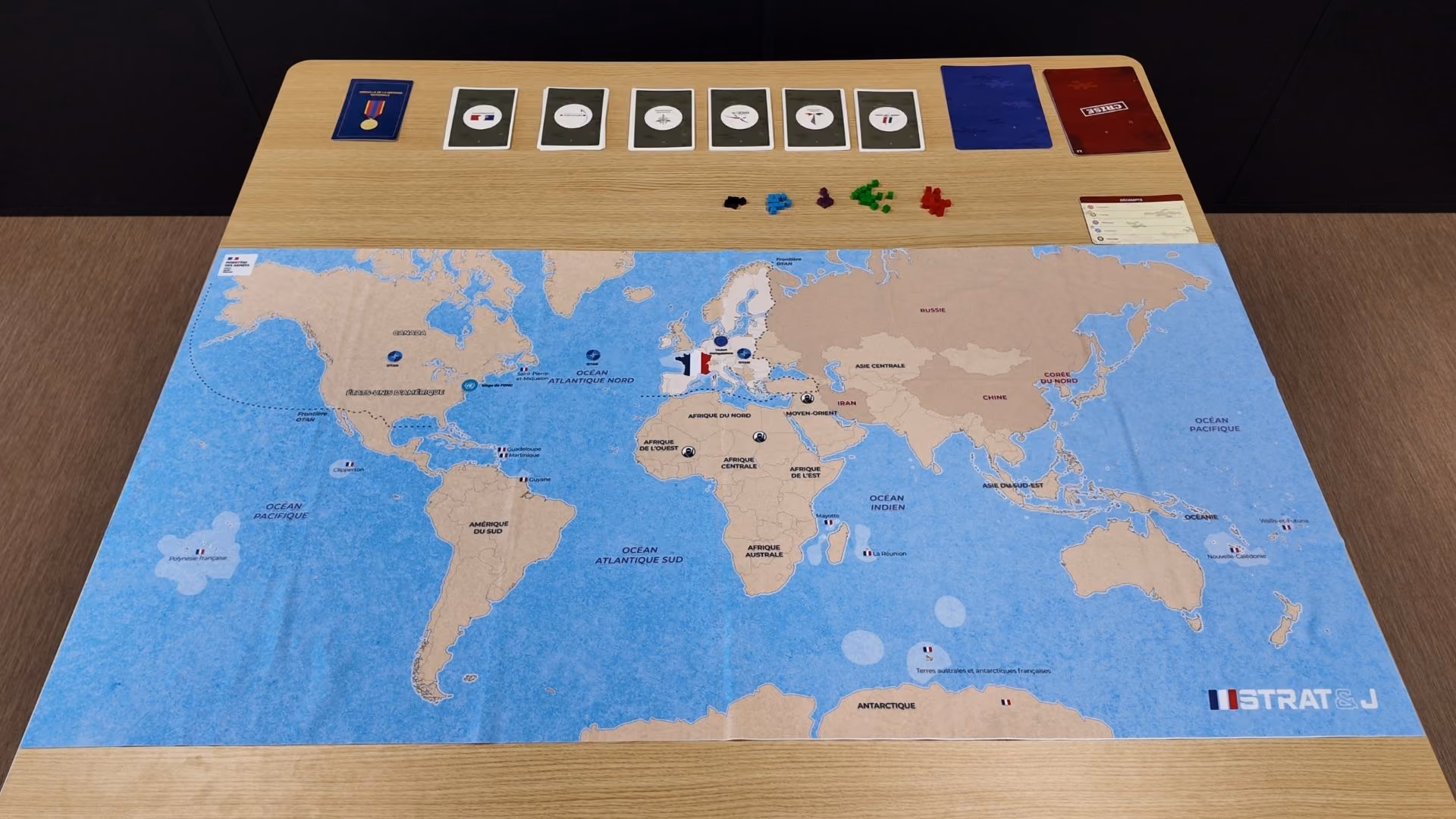 Mise en place complète du jeu Strat&J : grand plateau carte du monde avec territoires français, cartes armées, cubes et fiche de décompte