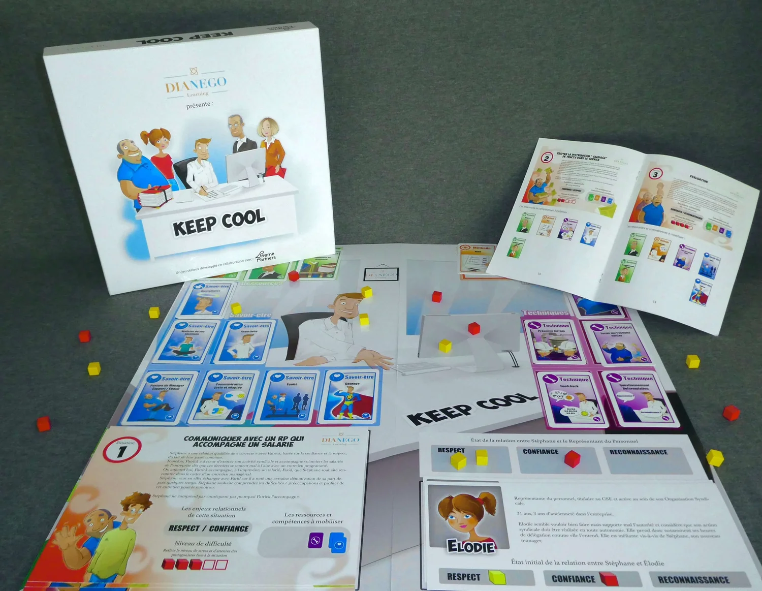 Mise en place du jeu Keep Cool : boîte éditée par Dianego, livret ouvert, plateaux, fiches personnages et cubes de couleur