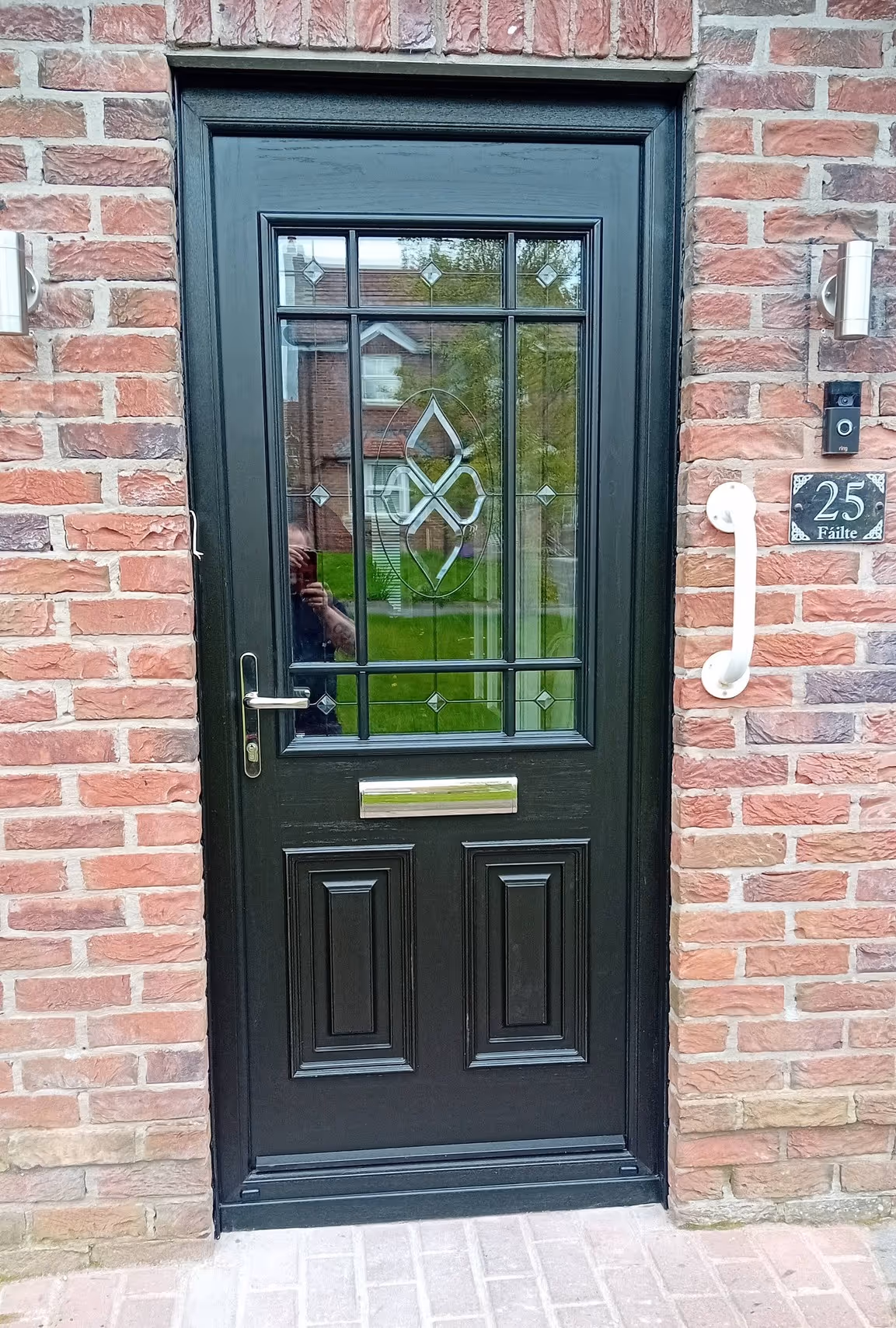Black composite front door with decorative glass fitted on a brick house