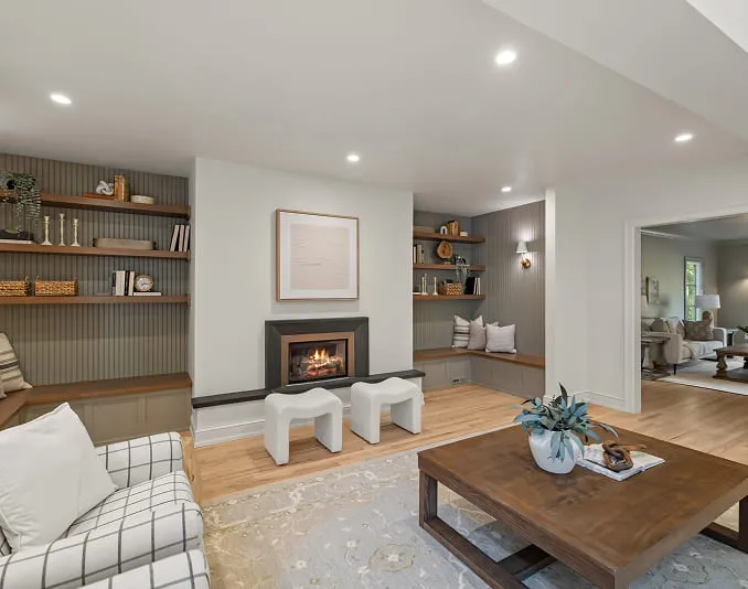 Cozy living room with fireplace, built-in shelves, cushioned benches, plaid armchair, and a wooden coffee table.