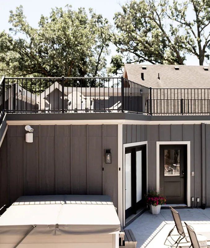 Modern dark gray house exterior with rooftop deck, white patio furniture, and potted flowers near door.