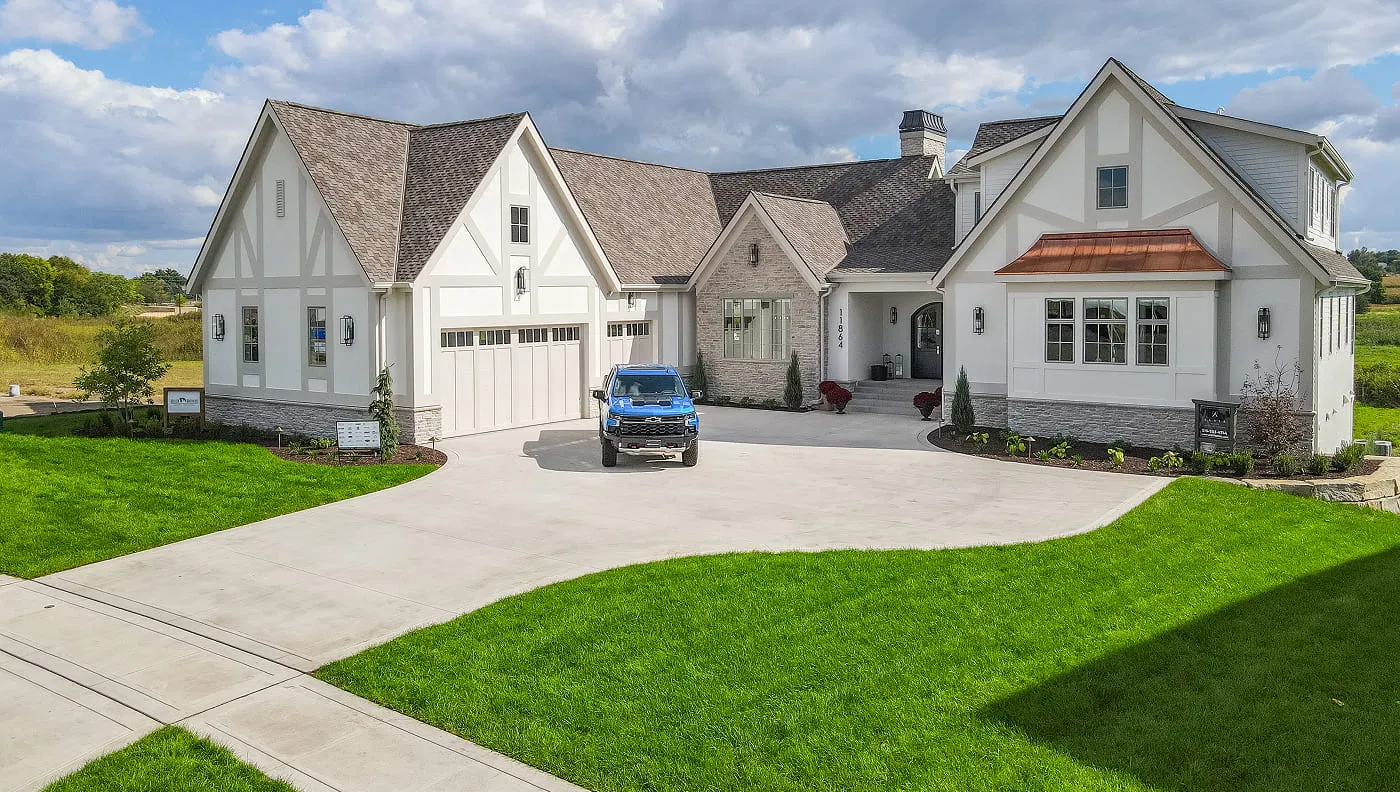 Large Tudor-style house with steep roof, light exterior, and blue truck parked on driveway.