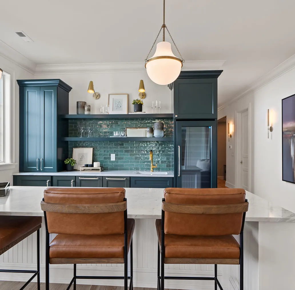 Modern kitchen with blue cabinets, green tile backsplash, white marble island, and brown leather bar stools.