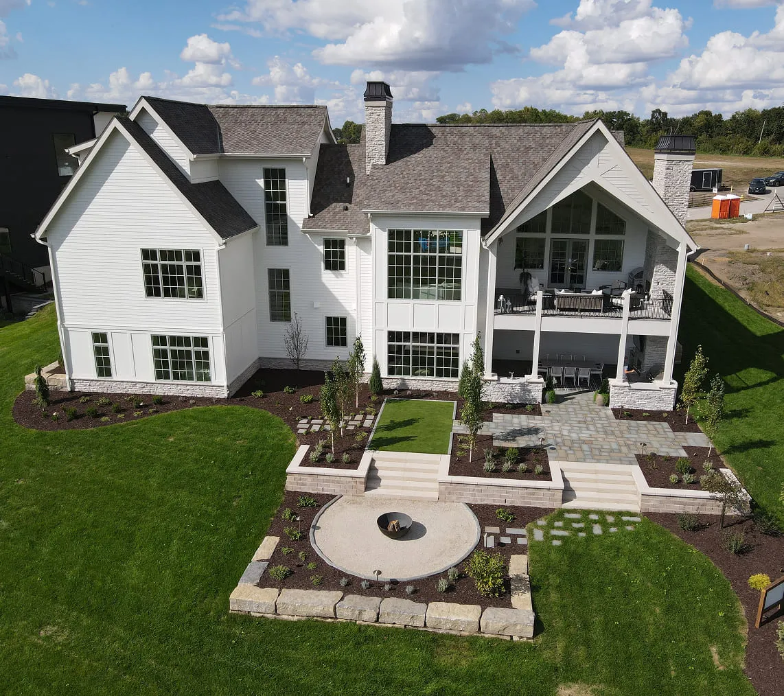 Large white house with multiple gables, stone chimney, patio, and landscaped yard with fire pit.