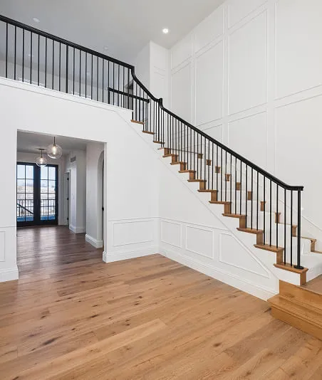 Bright interior featuring wooden staircase with black railing and light wood flooring.