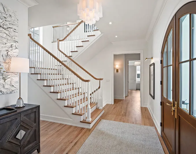 Bright home entry with wooden stairs, white railings, chandelier, wood floor, and large arched front door.