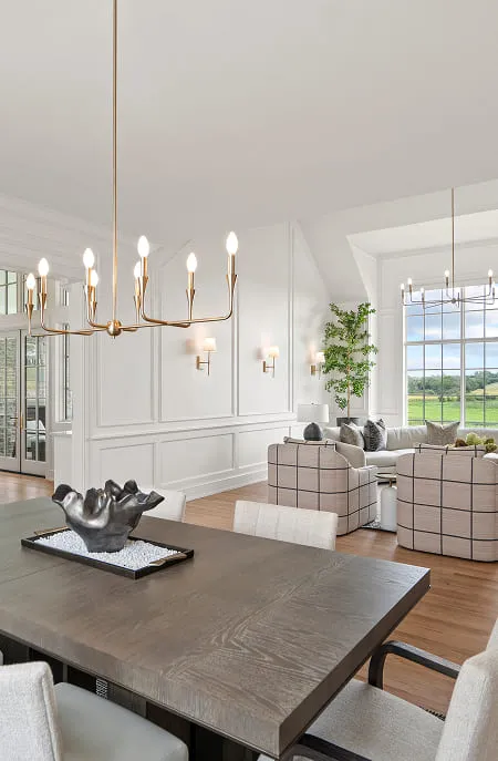 Modern dining area with wooden table, sculptural centerpiece, and adjacent bright living room with large window.