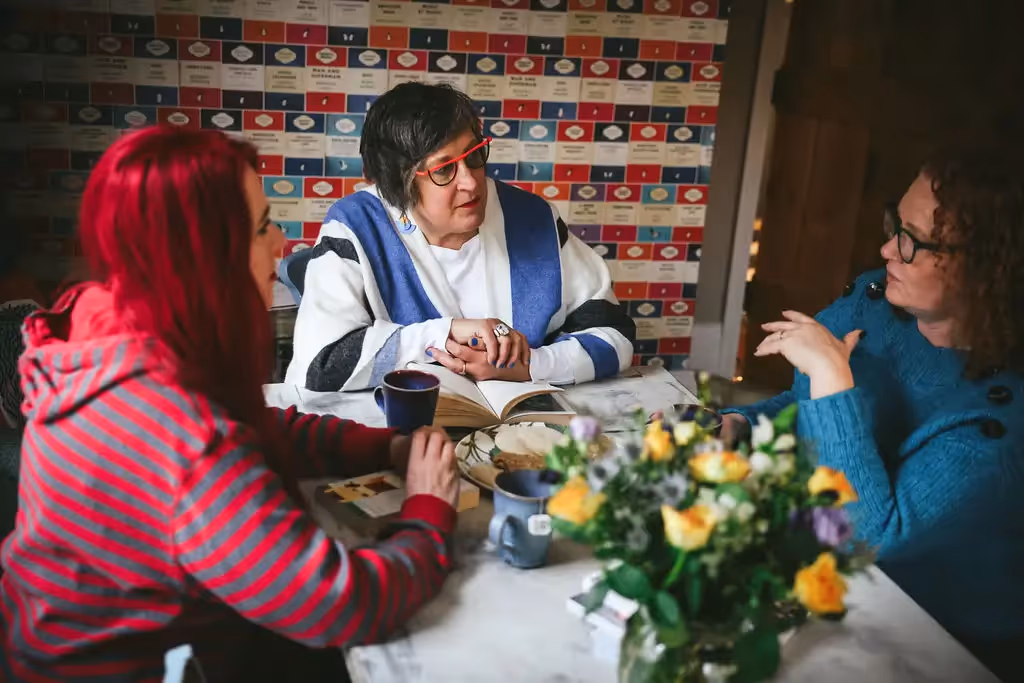 Three women talking around a table with spring flowers in a rustic room