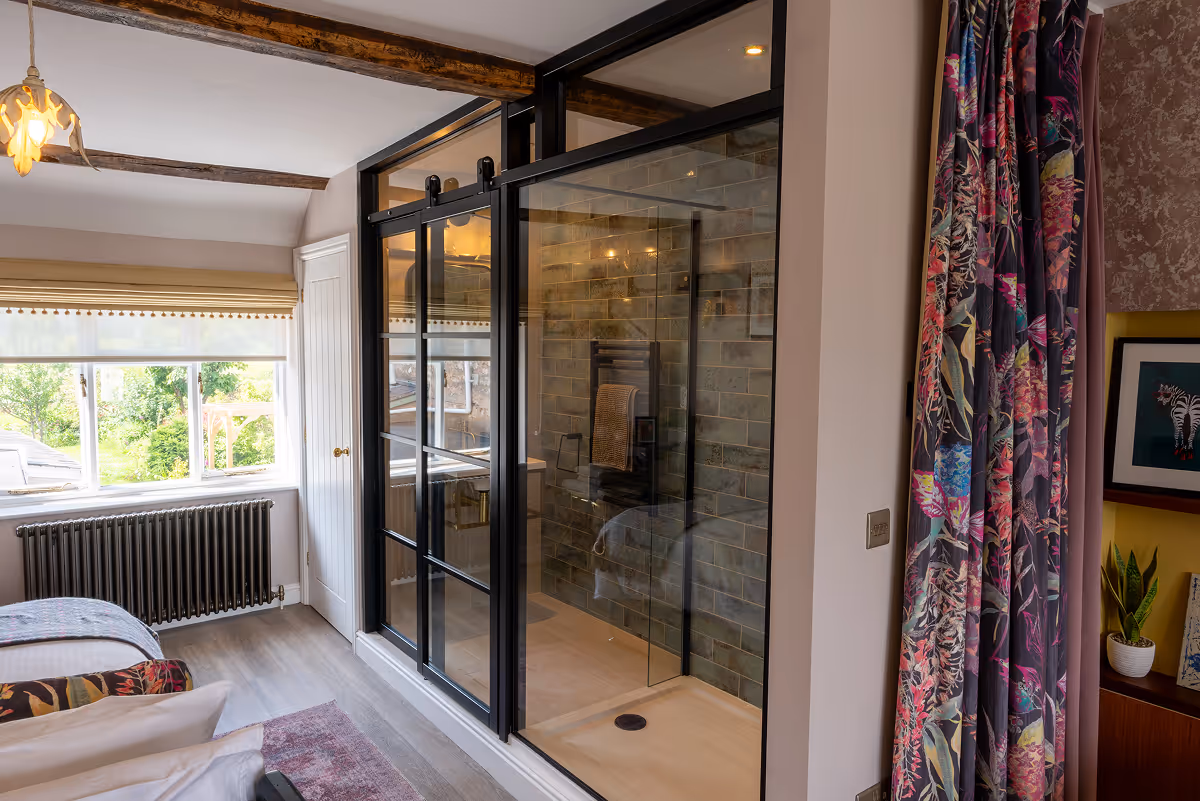Bedroom with glass-walled walk-in shower beside a window and floral curtains