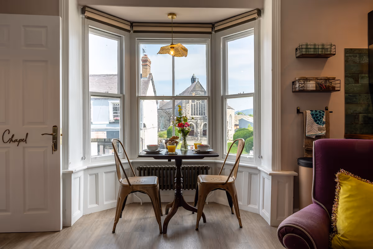 Dining table set in a bay window with rooftop town views