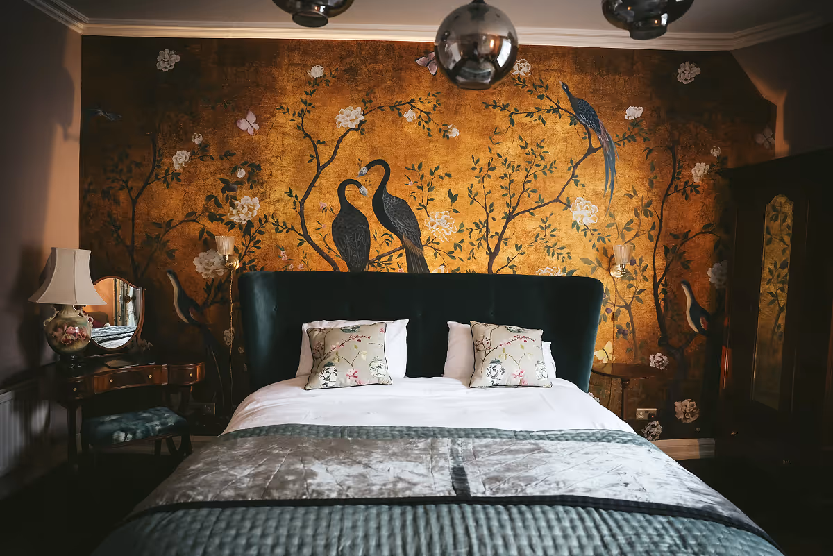 Luxurious bedroom with gold floral peacock mural behind a dark upholstered bed