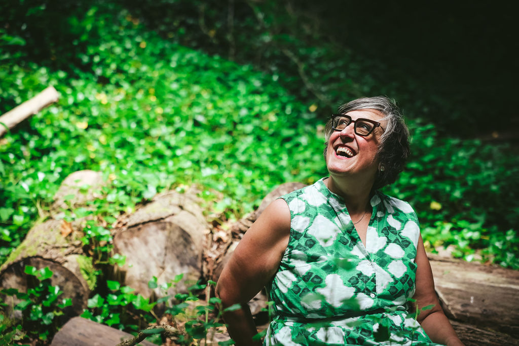 Woman in green dress laughing in a lush green woodland