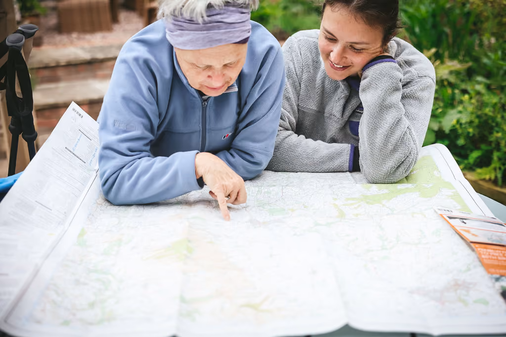 Two women in fleece jackets looking at and pointing to a large map outdoors.