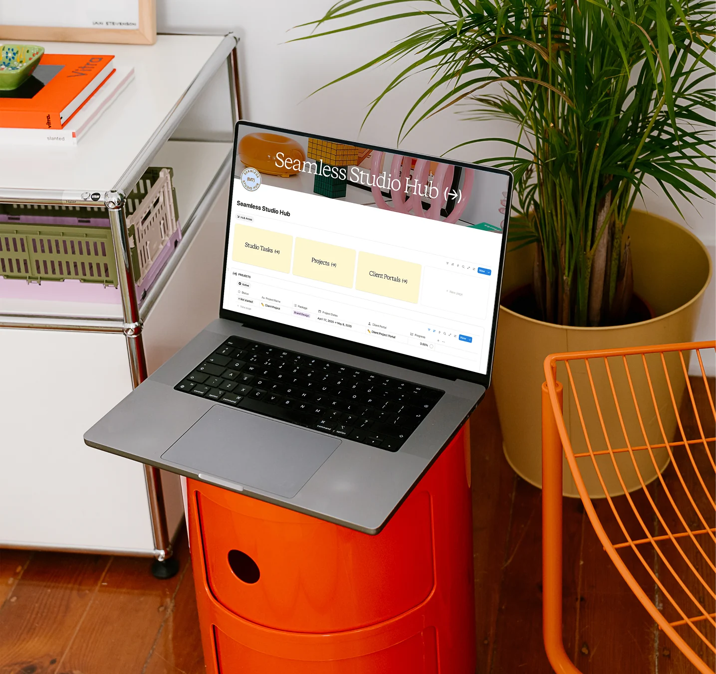 A laptop open on the Seamless Studio Hub dashboard, showing Studio Tasks, Projects and Client Portals, on an orange side table in a design studio