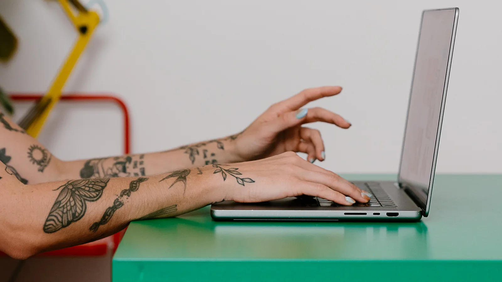 A website designer typing on a laptop at a green desk