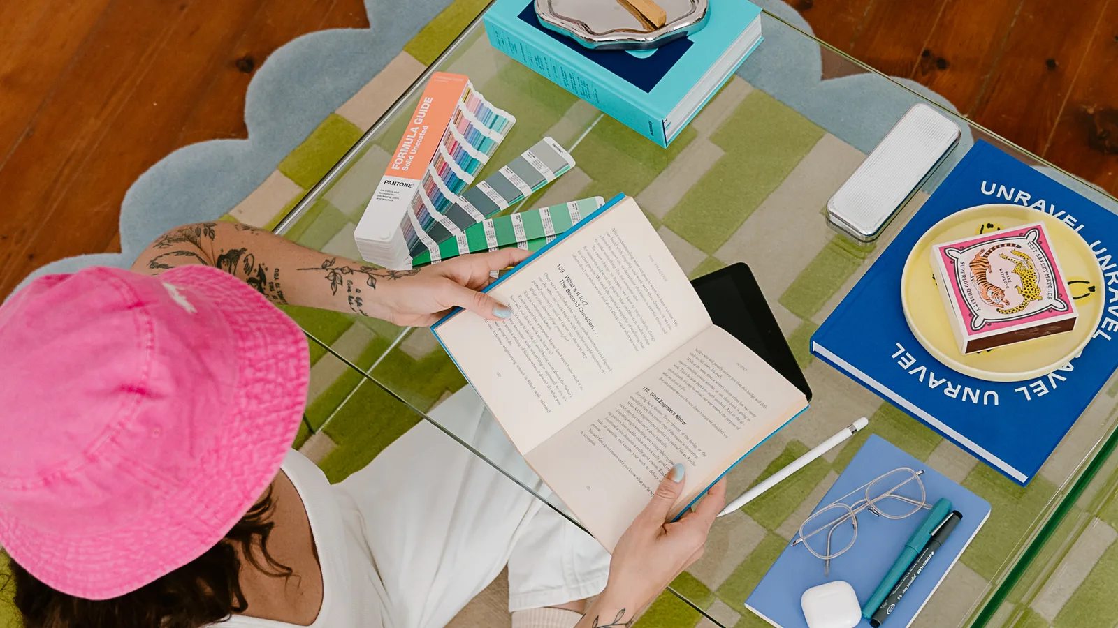 A brand designer reading at a glass coffee table, with Pantone swatches, books and a notebook laid out around her