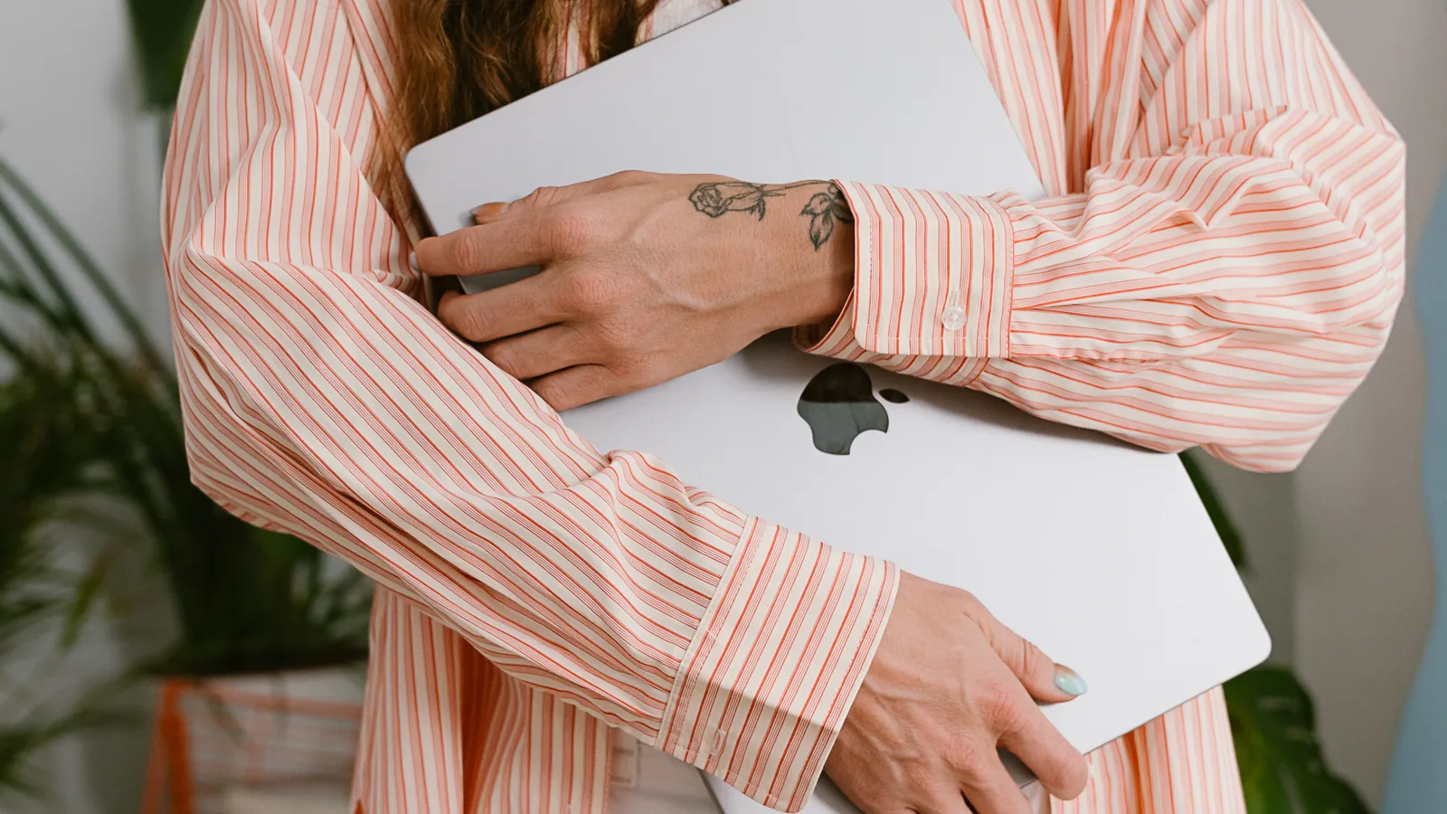 A design studio owner holding her laptop, wearing a pink striped shirt
