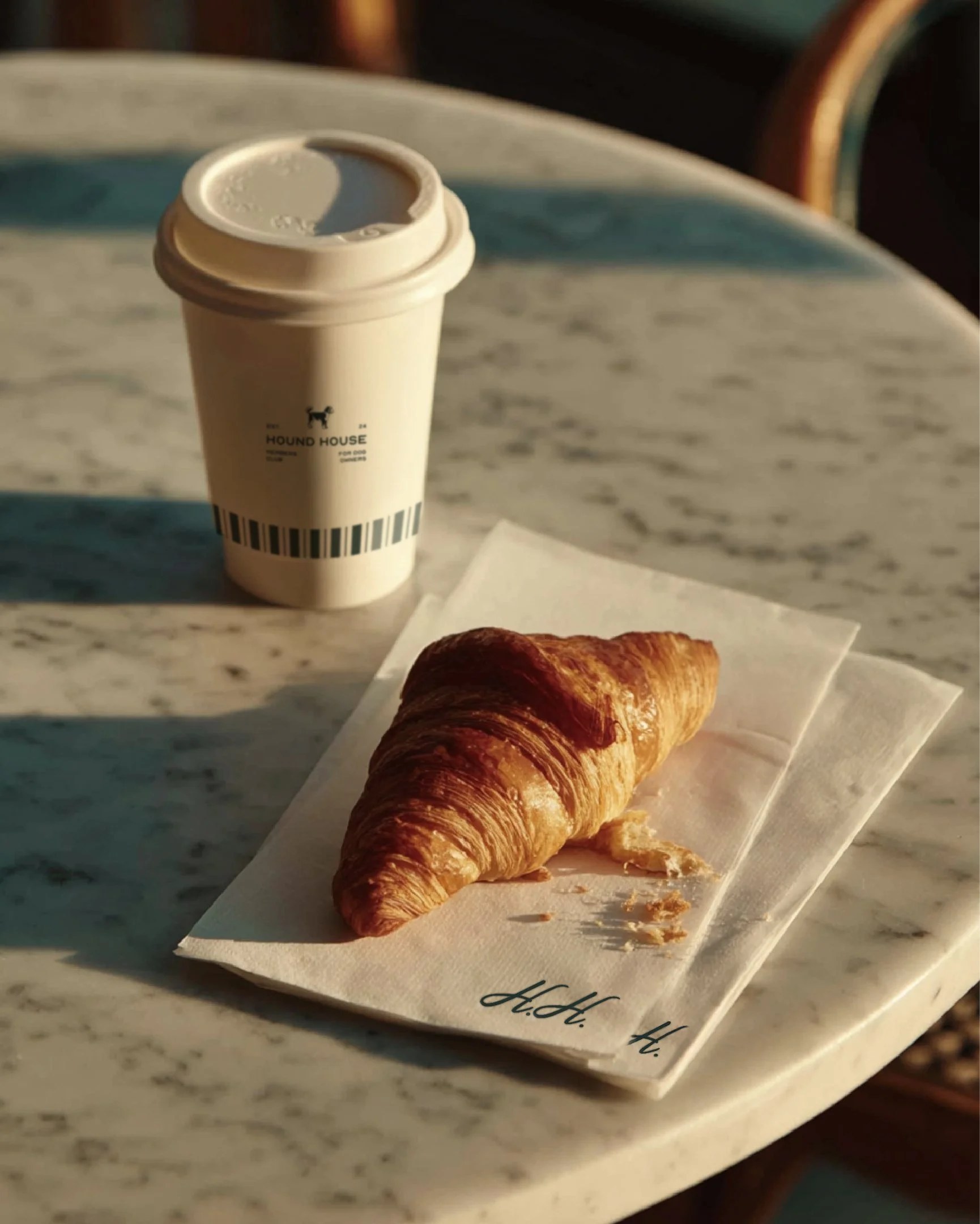 Hound House branded coffee cup and napkin on an outdoor table