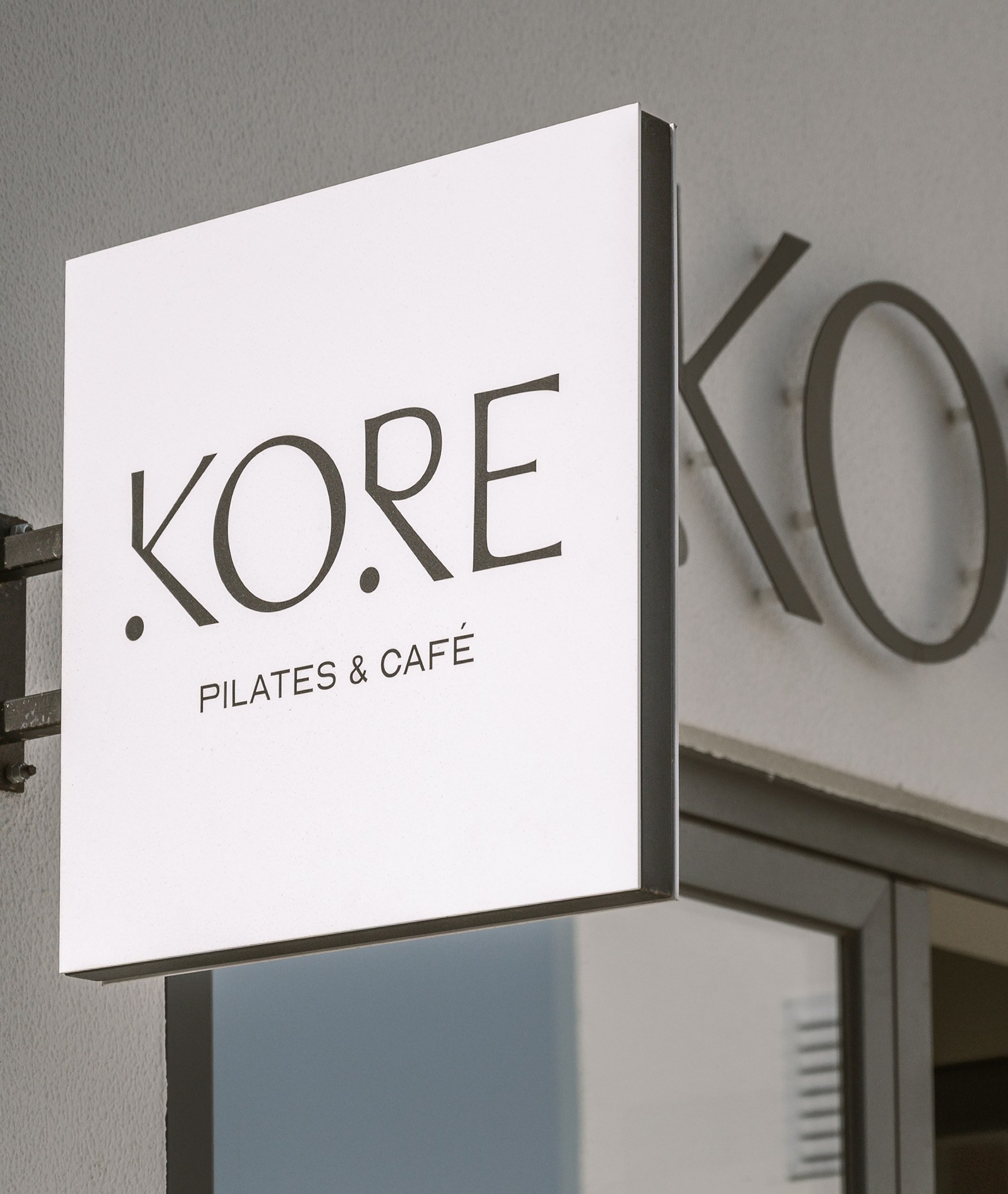 Kore Pilates A-frame sandwich board sign reading Pilates & Café in the studio's cream-and-black branding