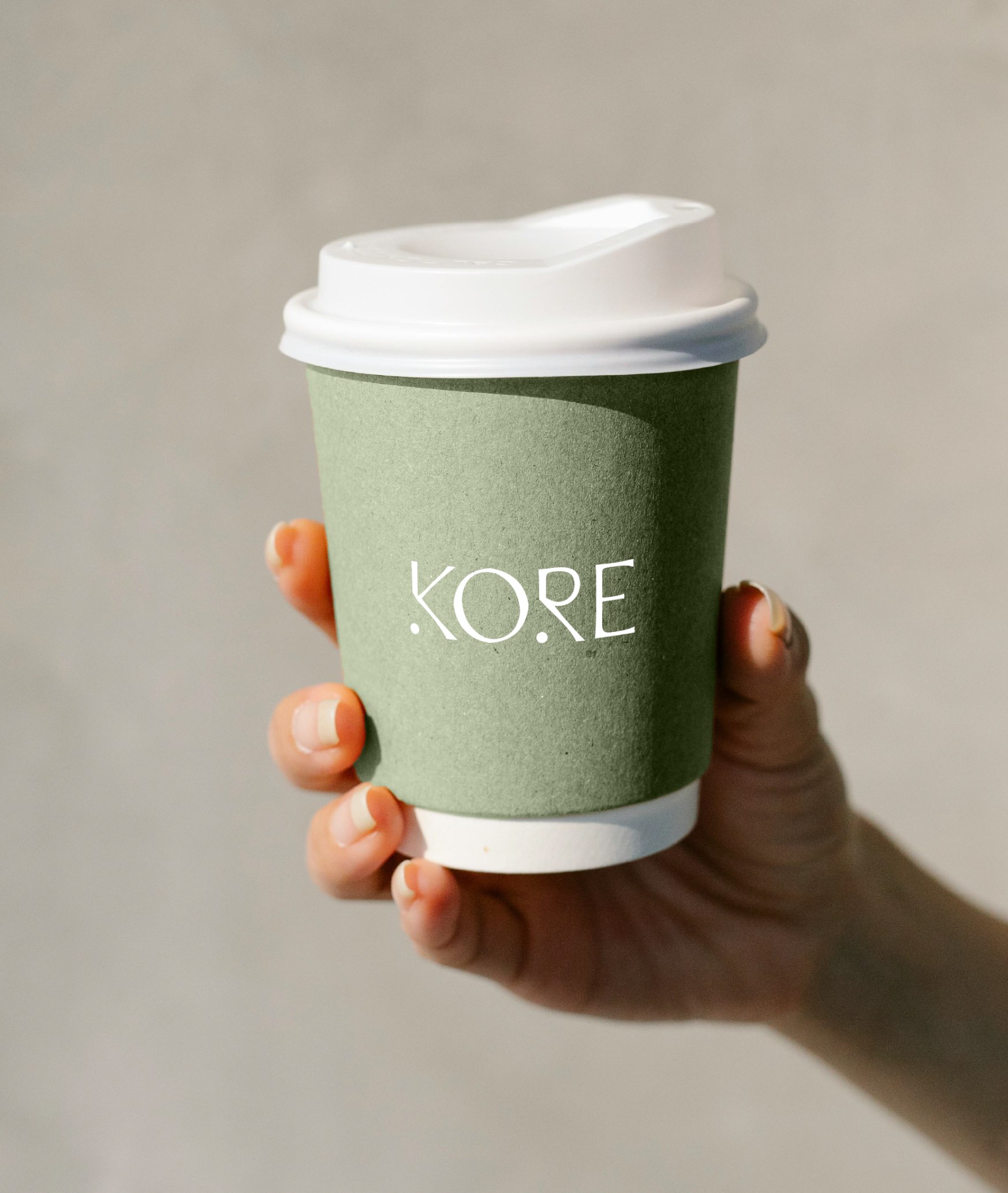 Kore Pilates branded takeaway coffee cup in sage green, held in hand