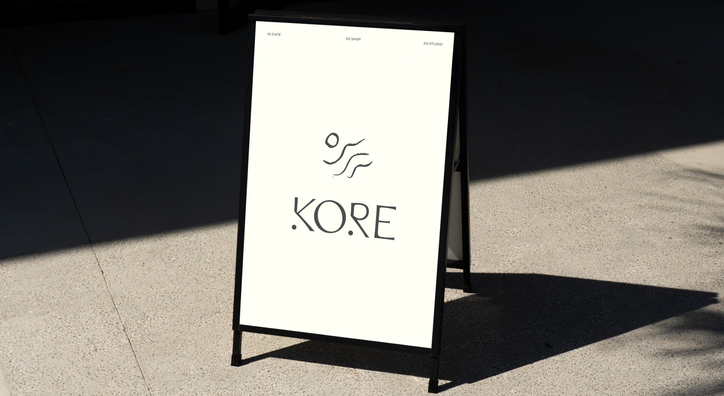 Kore Pilates A-frame pavement sign with the logo photographed on concrete in sunlight