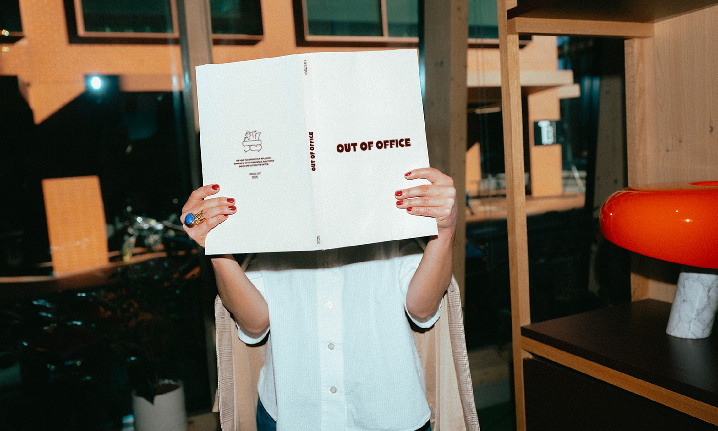 Out of Office printed brochure held in an interior with a red stool