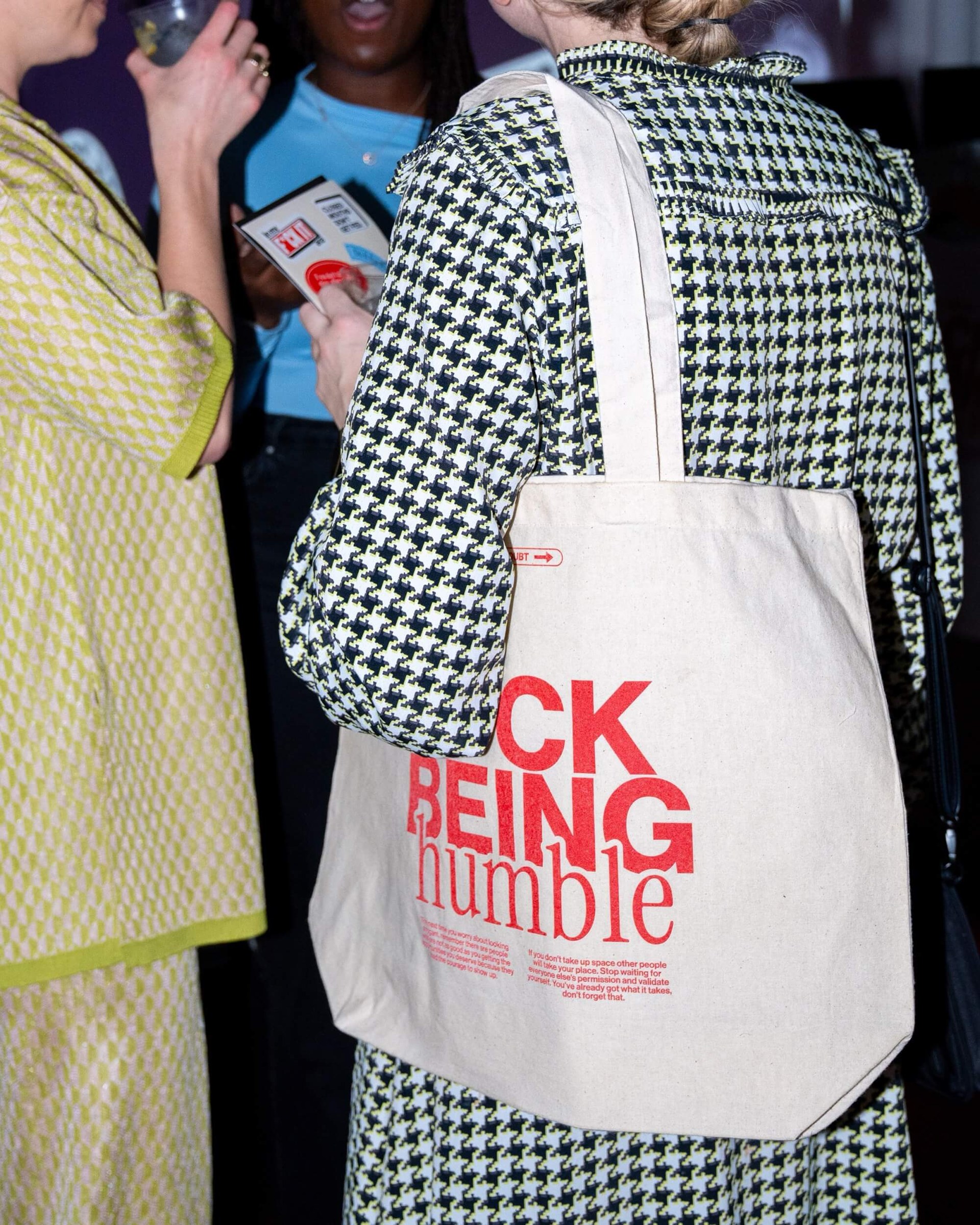 F*ck Being Humble tote bag held by a person in a checked coat