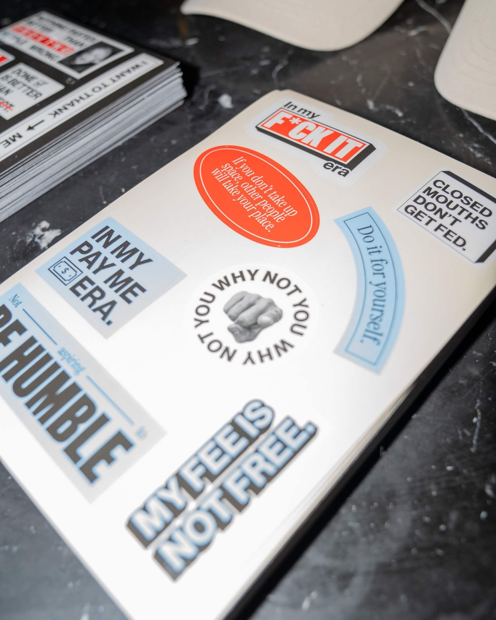 F*ck Being Humble round sticker coasters on a concrete ledge